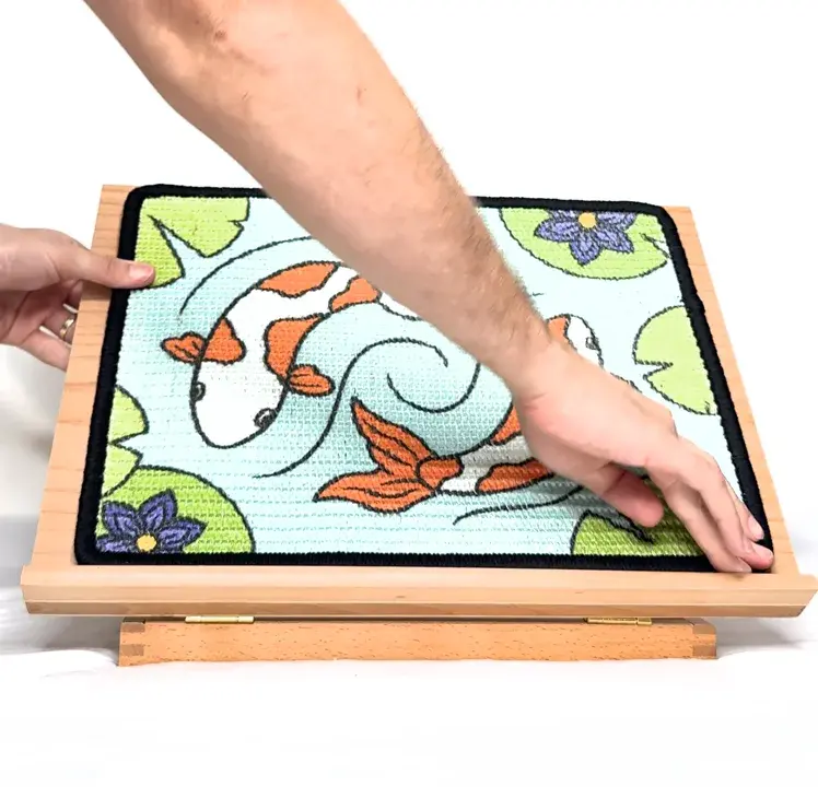 Two hands pressing the Koi scratch panel down onto the wooden easel.