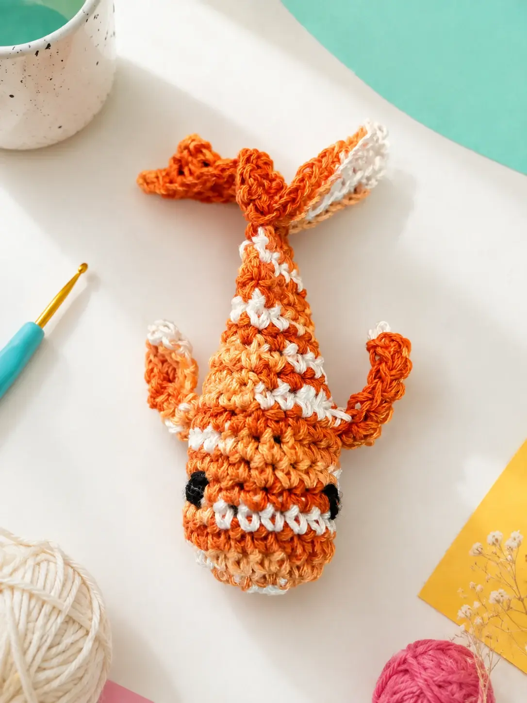 Orange-and-white hand-crocheted koi fish cat toy in an art studio setting.