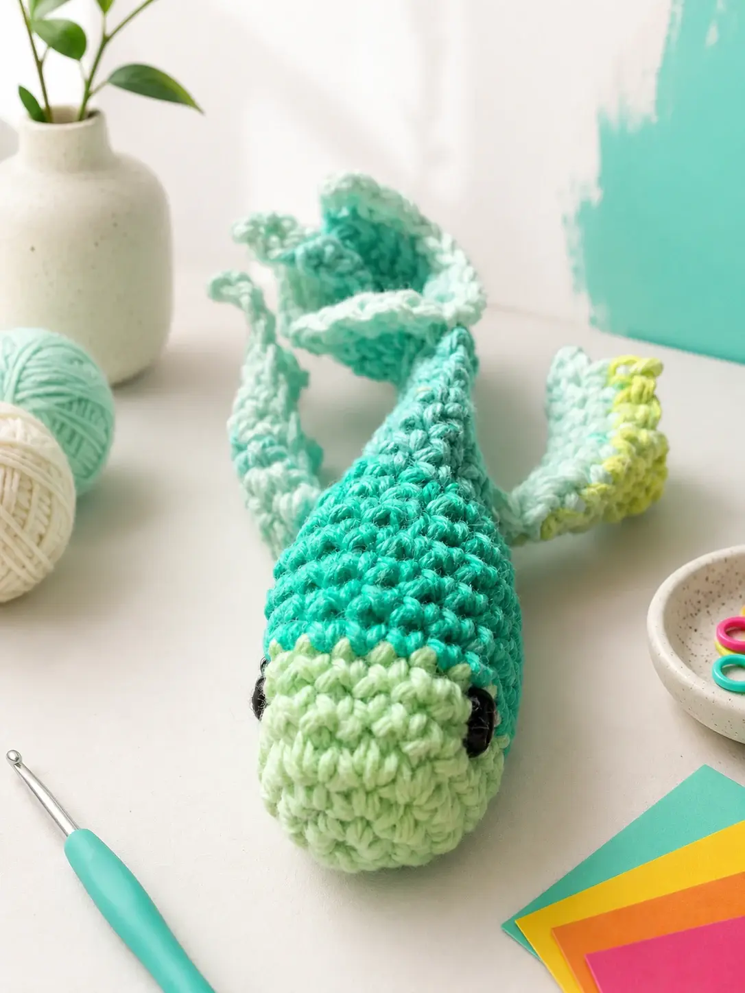 Teal-and-mint hand-crocheted koi fish cat toy in an art studio setting.