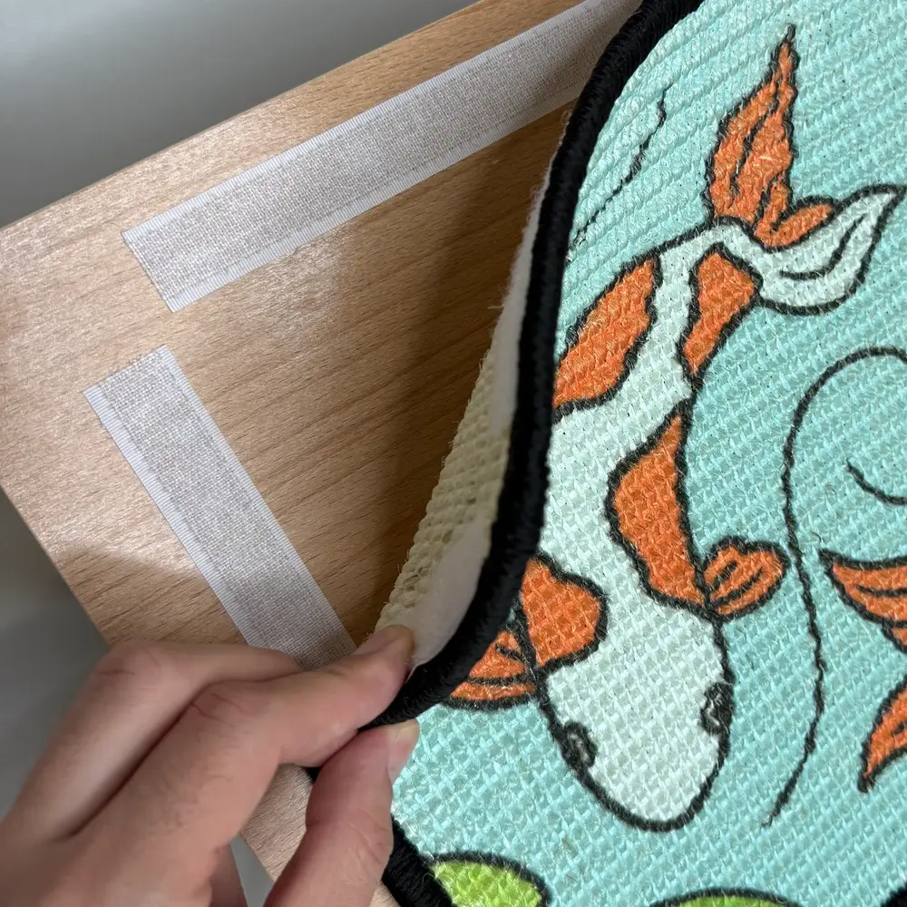 Hand lifting the Koi scratch panel from the wooden easel, showing the hook-and-loop fastening strips underneath.